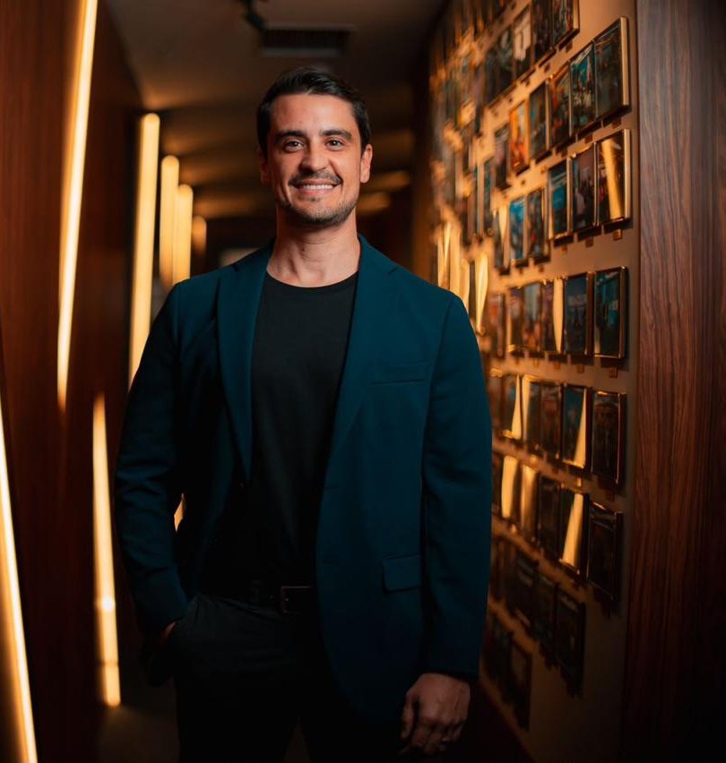 Retrato do Dr. Rafael Roldão sorrindo, de blazer, num corredor com painéis de madeira iluminados